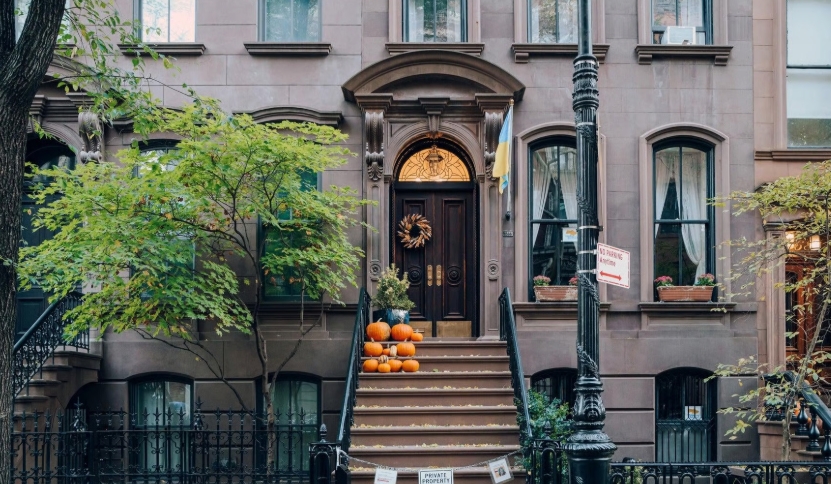 De brownstone-entree van Carrie Bradshaws appartement met een buitentrap en pompoenen.