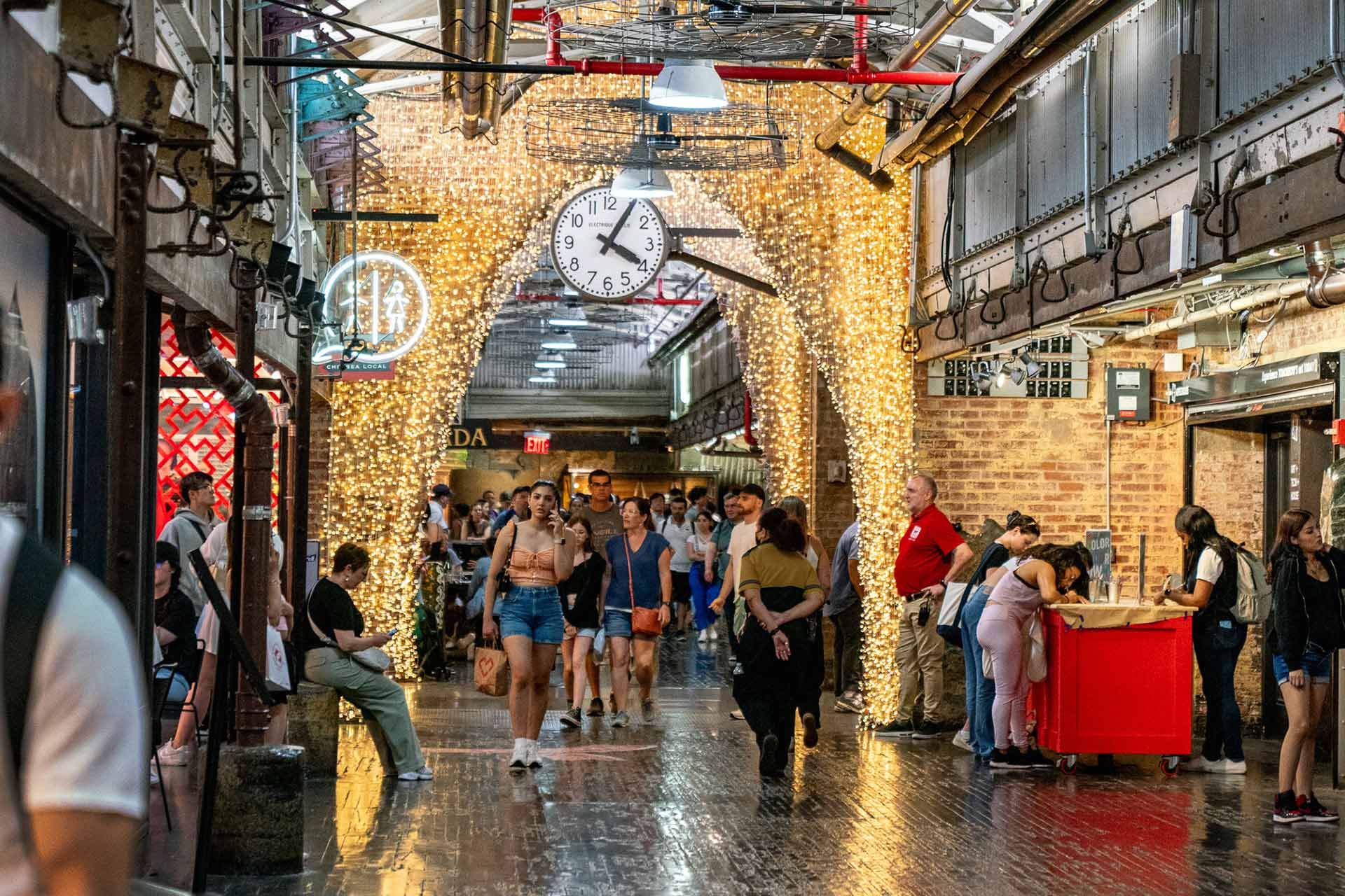 Bezoekers onder de verlichte boog met de grote klok in Chelsea Market.