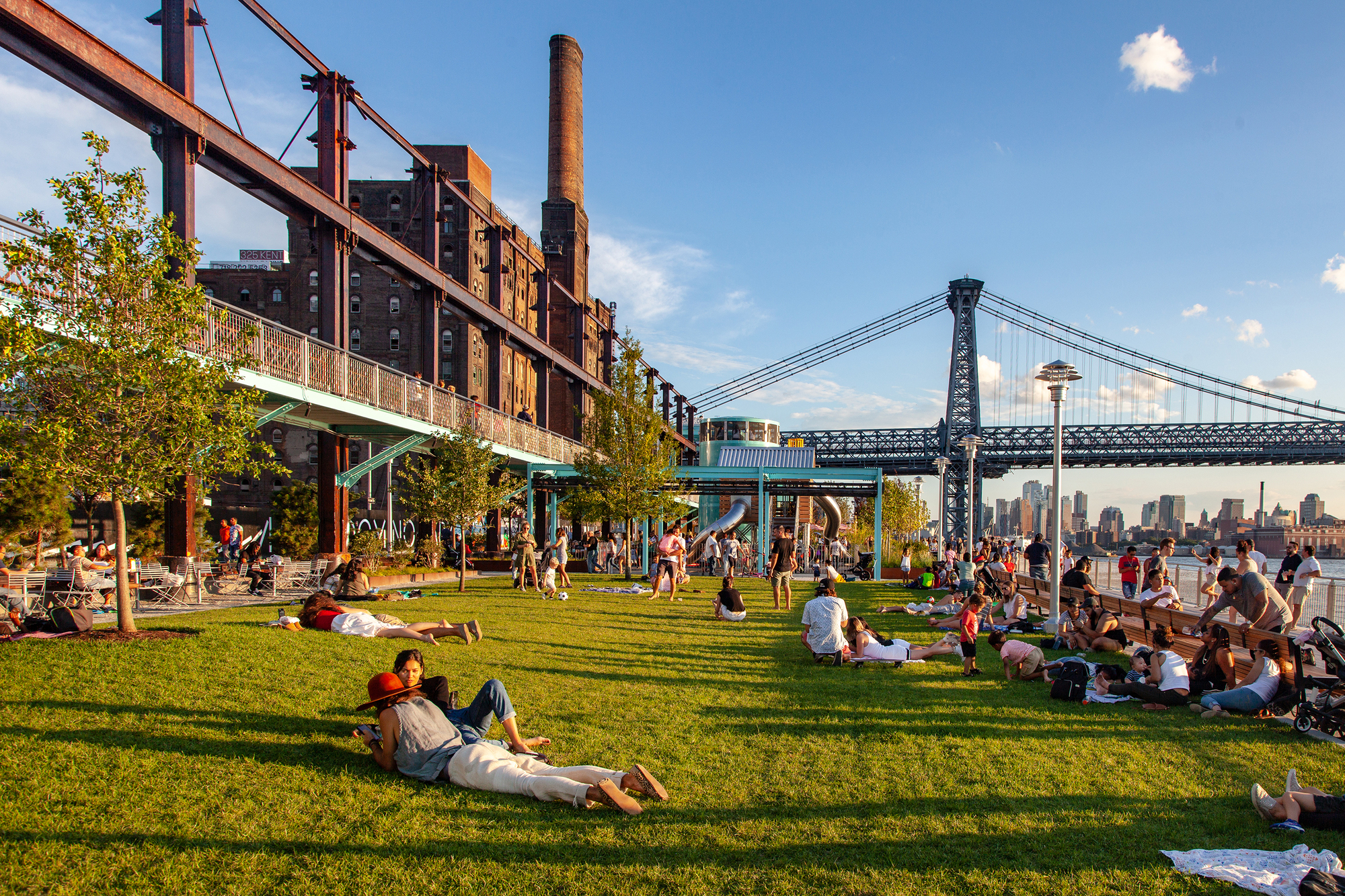 Bezoekers op het grasveld van Domino Park, naast de oude suikerfabriek en de Williamsburg Bridge.