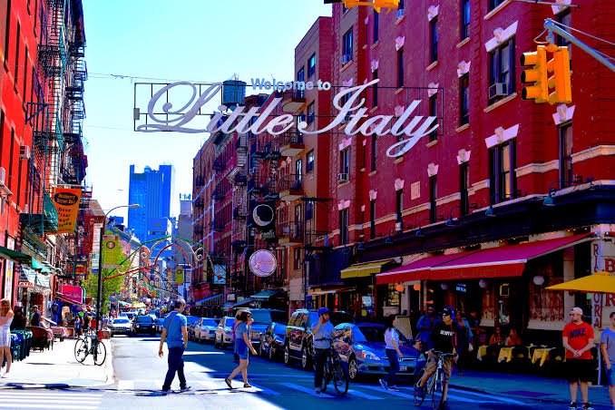 Een straat in Little Italy met restaurants, bezoekers en het bord Welcome to Little Italy.