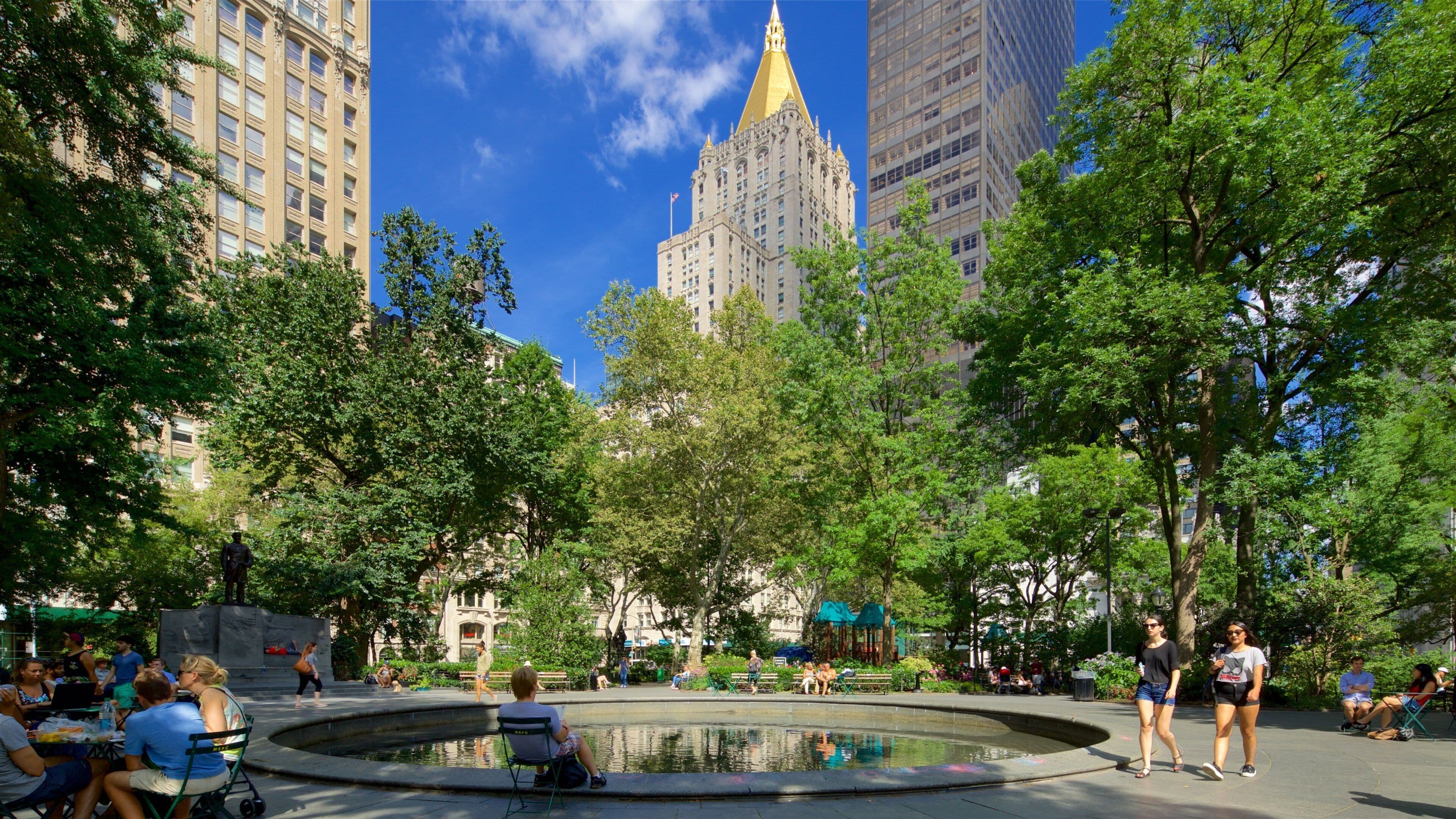 De ronde fontein in Madison Square Park, met bomen en het goudkleurige dak van het New York Life Building.