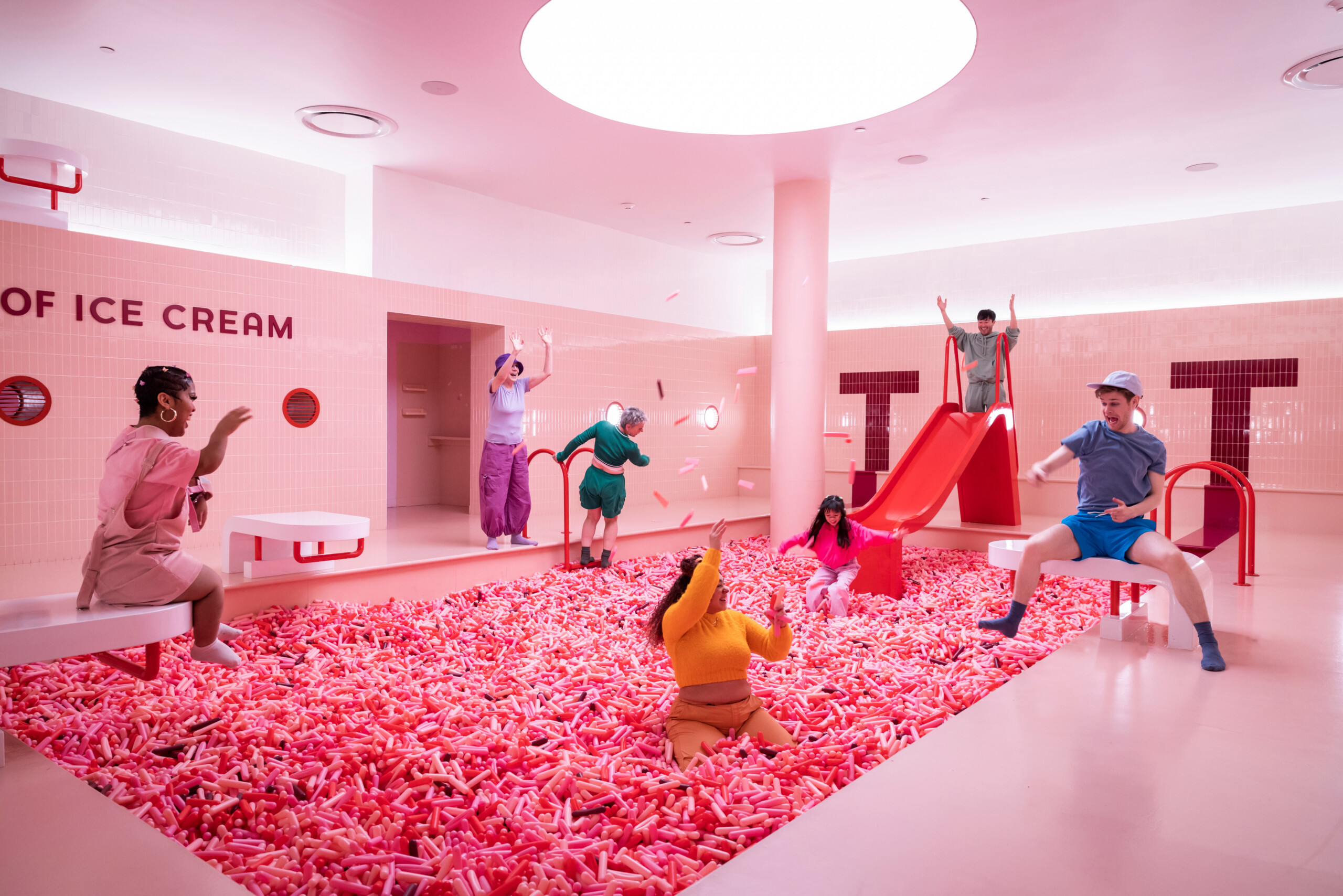 Bezoekers in het roze sprinklesbad van het Museum of Ice Cream, met een rode glijbaan.