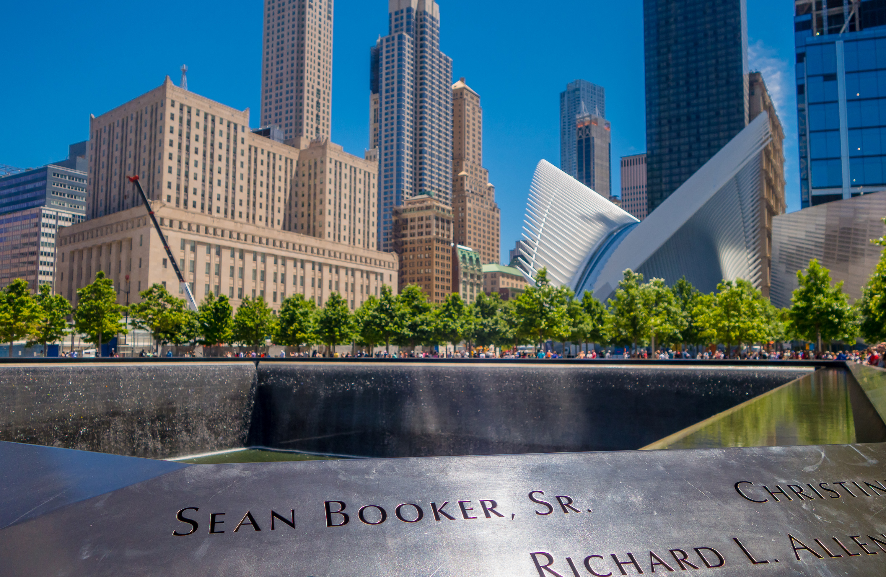 Het waterbassin van het 9/11 Memorial met namen in de bronzen rand en de Oculus op de achtergrond.
