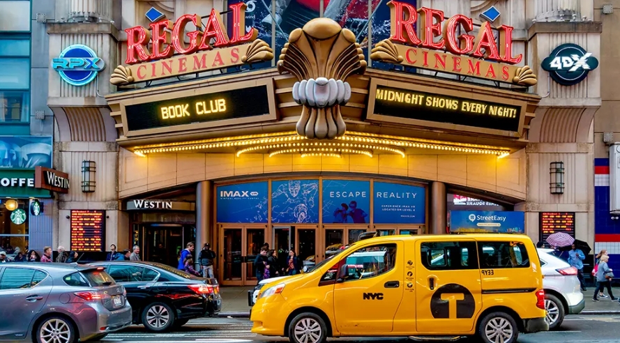 De verlichte gevel van Regal Cinemas aan Times Square met een gele taxi.