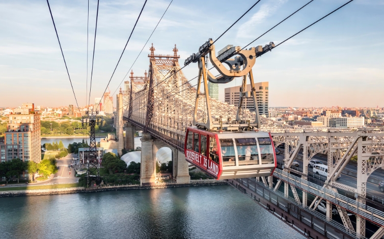 De rode Roosevelt Island Tramway-cabine boven de East River naast de Queensboro Bridge.