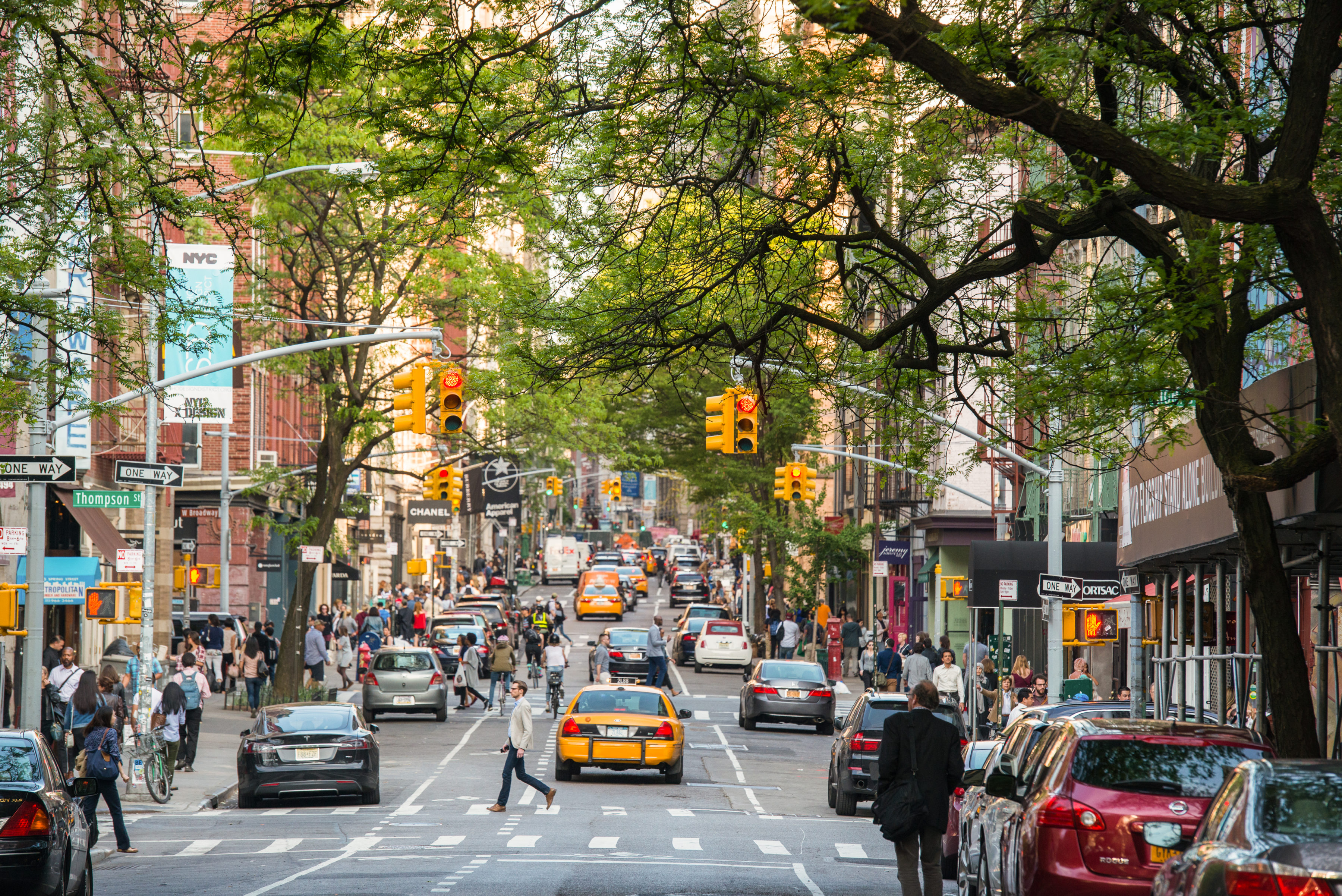 Een levendige straat in SoHo met bomen, winkels, voetgangers en gele taxi's.