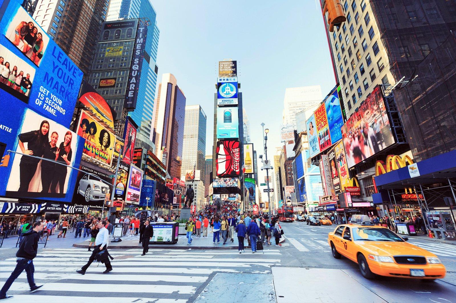Times Square met lichtreclames, voetgangers en een gele taxi.