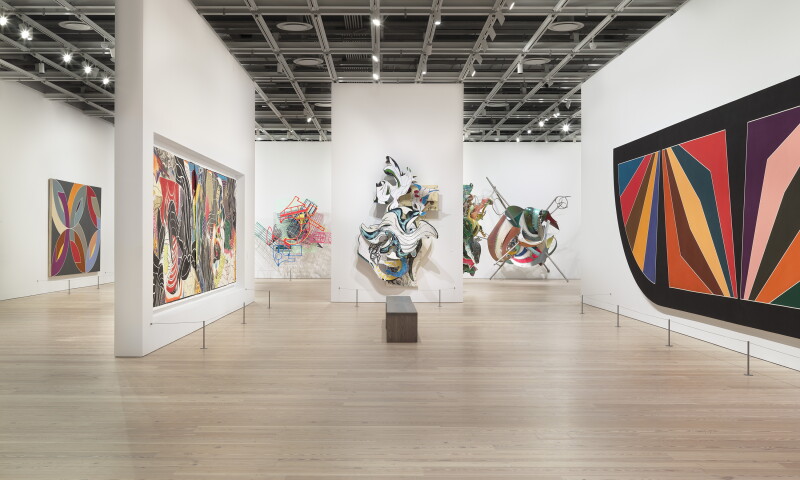 Een lichte zaal in het Whitney Museum met kleurrijke abstracte kunst en sculpturen.